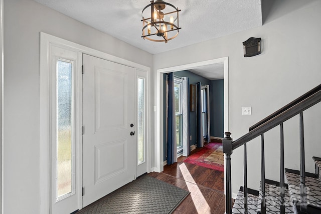 foyer with stairs, a textured ceiling, plenty of natural light, and a notable chandelier