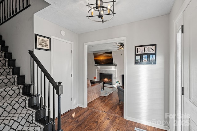 entryway featuring a warm lit fireplace, a textured ceiling, ceiling fan with notable chandelier, stairs, and dark wood finished floors