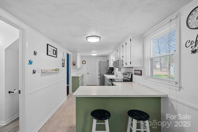 kitchen with appliances with stainless steel finishes, a breakfast bar, light countertops, and a peninsula