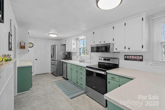 kitchen with stainless steel appliances, a sink, white cabinets, green cabinets, and light countertops