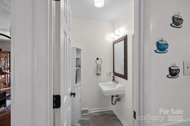 bathroom featuring a textured ceiling, a sink, and baseboards