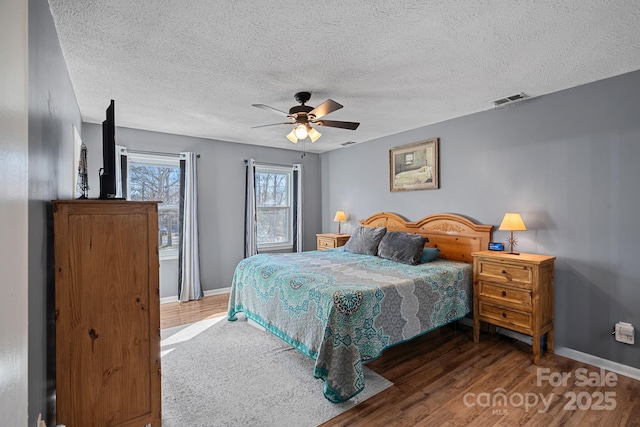 bedroom with ceiling fan, wood finished floors, visible vents, and baseboards