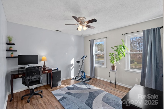 home office featuring baseboards, visible vents, ceiling fan, wood finished floors, and a textured ceiling