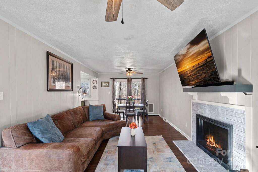 living room featuring ceiling fan, ornamental molding, a fireplace, a textured ceiling, and dark wood-style flooring