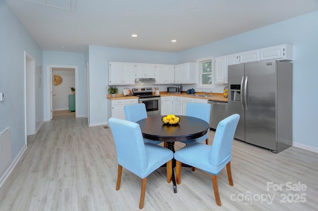 kitchen with light countertops, light wood-style flooring, appliances with stainless steel finishes, white cabinetry, and under cabinet range hood