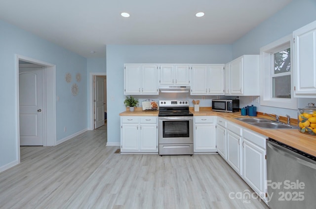 kitchen with appliances with stainless steel finishes, light wood-type flooring, white cabinetry, and a sink