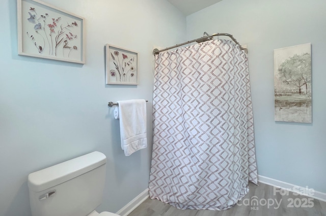 bathroom featuring toilet, curtained shower, baseboards, and wood finished floors