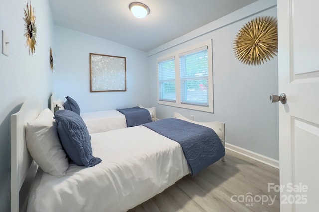 bedroom with vaulted ceiling, wood finished floors, and baseboards