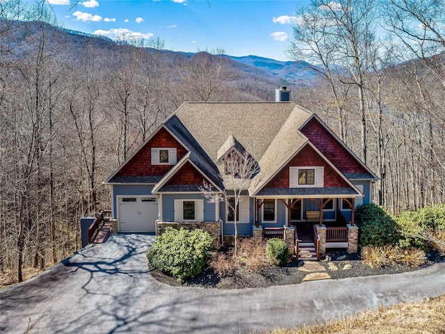 craftsman inspired home with a garage, a forest view, aphalt driveway, covered porch, and a mountain view