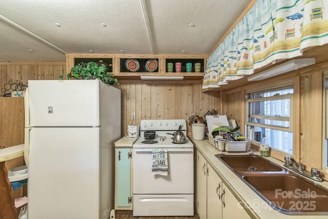 kitchen with open shelves, a sink, wood walls, a textured ceiling, and white appliances