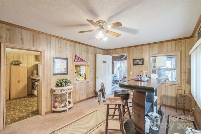 dining room featuring a textured ceiling, ornamental molding, carpet flooring, and wooden walls