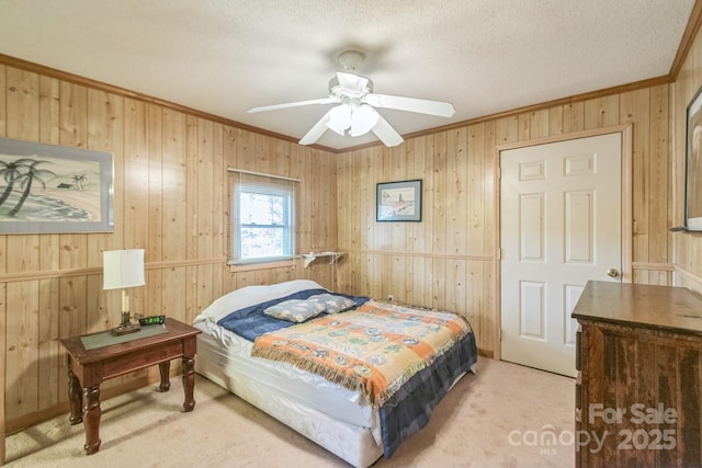 bedroom with light colored carpet, ceiling fan, a textured ceiling, crown molding, and wood walls