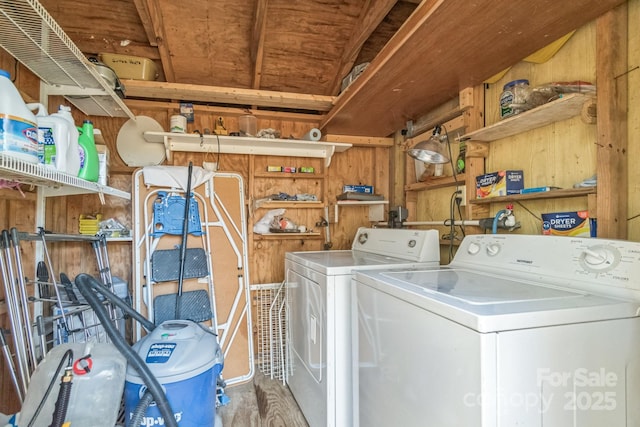 clothes washing area with laundry area, wooden walls, and washer and clothes dryer