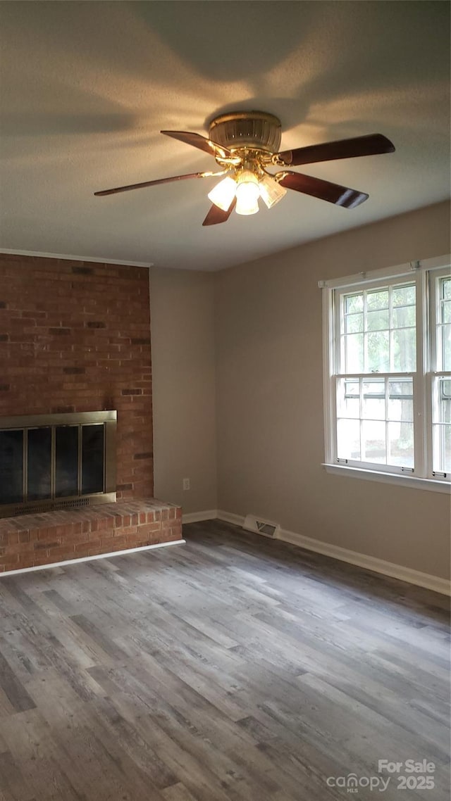 unfurnished living room featuring wood finished floors, visible vents, baseboards, a textured ceiling, and a brick fireplace