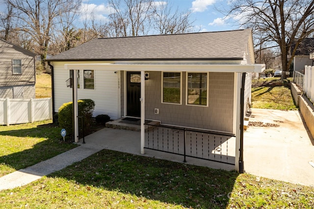 bungalow featuring a shingled roof, fence, and a front lawn