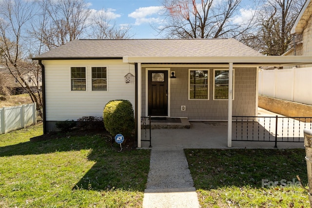 view of front of home featuring roof with shingles, fence, and a front yard