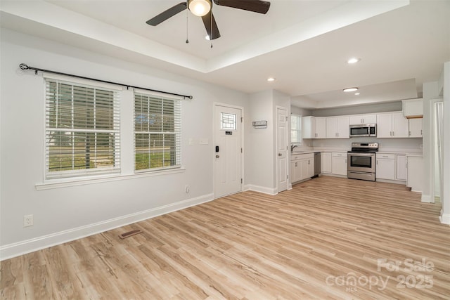 kitchen with baseboards, a raised ceiling, light wood-style flooring, appliances with stainless steel finishes, and white cabinetry