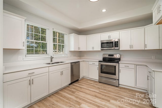 kitchen with light countertops, light wood-style flooring, appliances with stainless steel finishes, white cabinets, and a sink