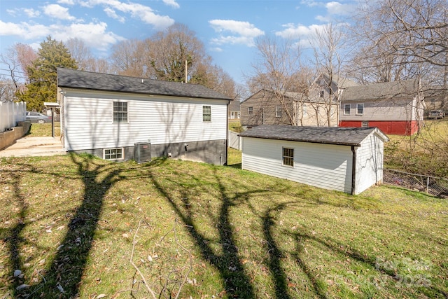 rear view of house featuring central AC unit, fence, an outbuilding, and a yard