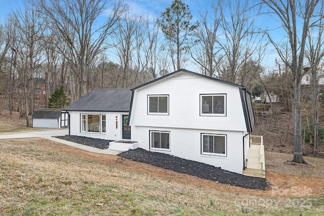 tri-level home with brick siding, roof with shingles, a gambrel roof, a front yard, and an outdoor structure