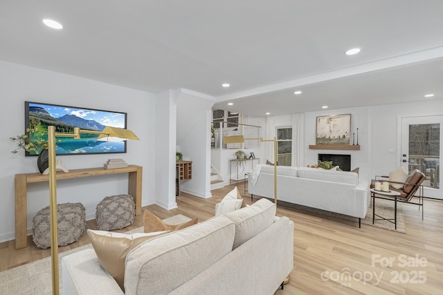 living room featuring light wood-type flooring, a fireplace, recessed lighting, and stairs