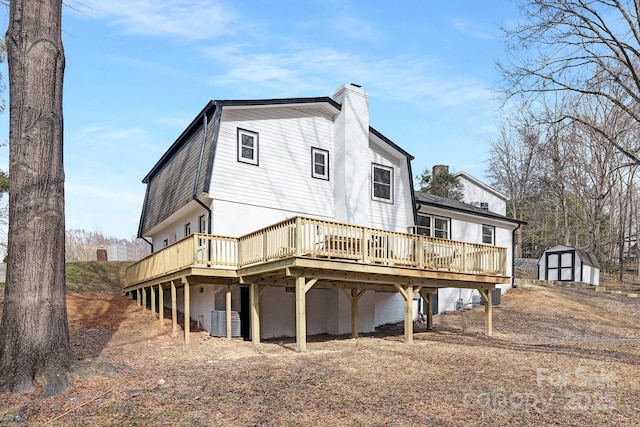 back of property featuring a deck, an outbuilding, a storage shed, a gambrel roof, and a chimney