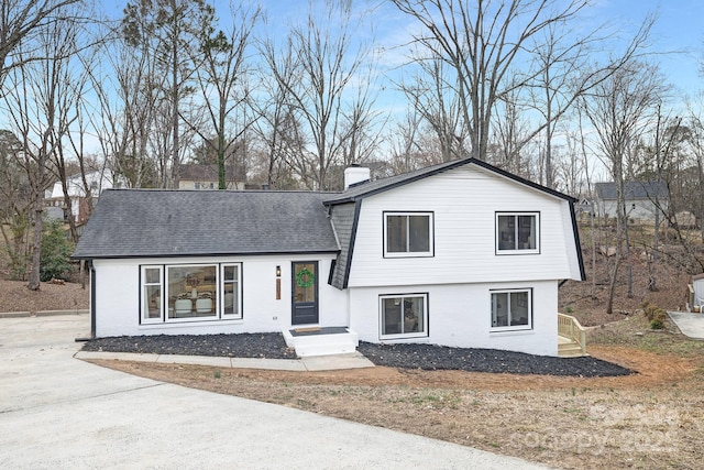 tri-level home with a shingled roof, a chimney, and brick siding