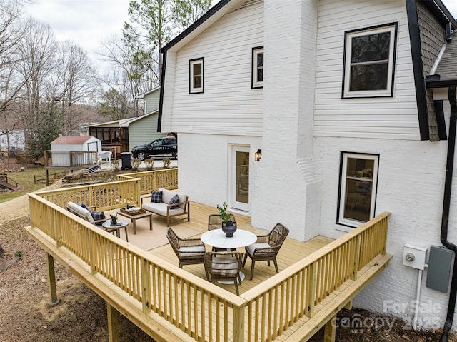 rear view of property with brick siding, an outdoor structure, an outdoor living space, and a wooden deck