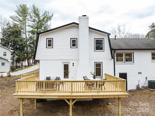 back of house with a shingled roof, a chimney, central AC unit, and brick siding