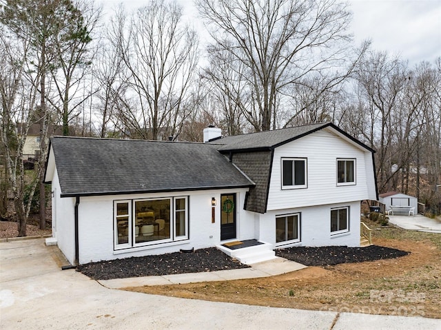 tri-level home with brick siding, a chimney, and roof with shingles