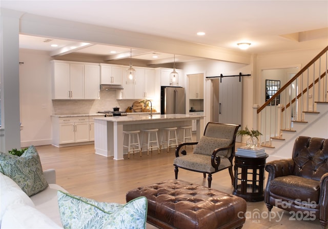 living room with a barn door, recessed lighting, light wood-style floors, stairs, and beam ceiling