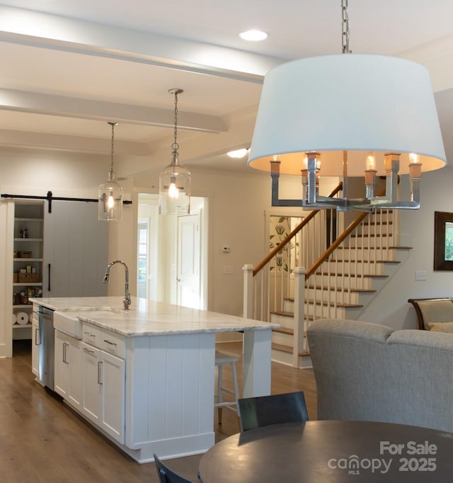 kitchen featuring dark wood-style flooring, stainless steel dishwasher, a barn door, white cabinetry, and a sink