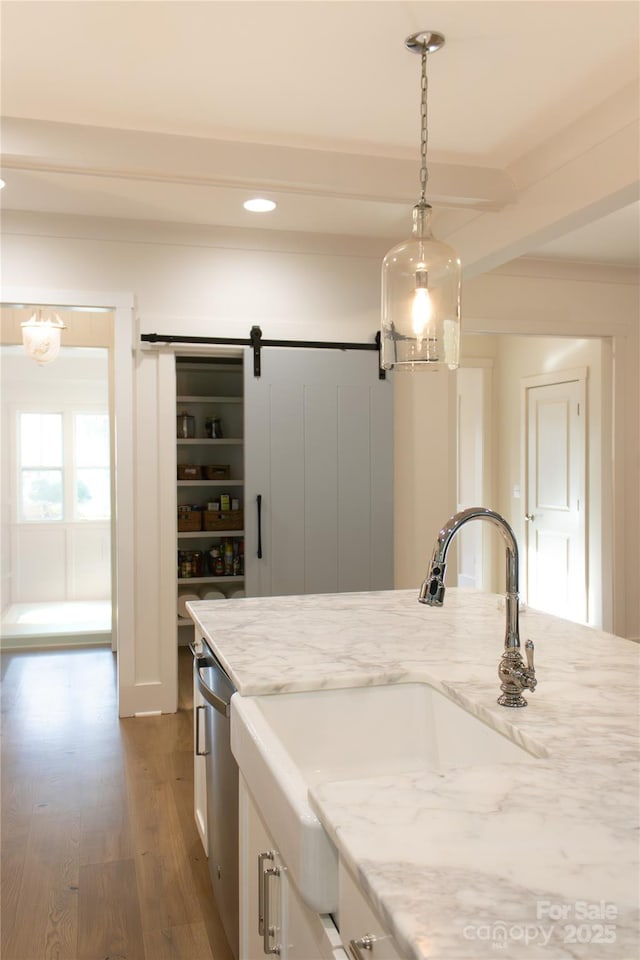 kitchen with a barn door, wood finished floors, white cabinetry, dishwasher, and pendant lighting