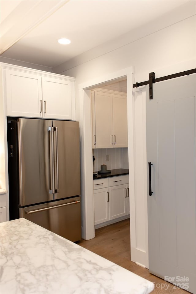 kitchen with high end fridge, a barn door, white cabinetry, and decorative backsplash