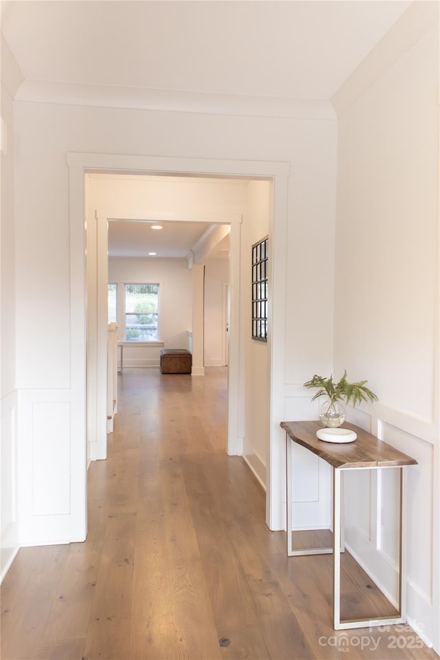 corridor featuring a decorative wall, wainscoting, wood finished floors, and crown molding