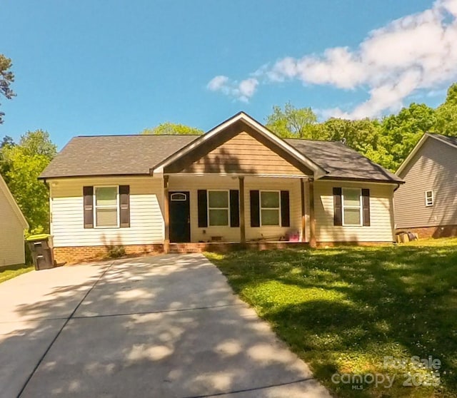 ranch-style home featuring covered porch, concrete driveway, roof with shingles, and a front lawn