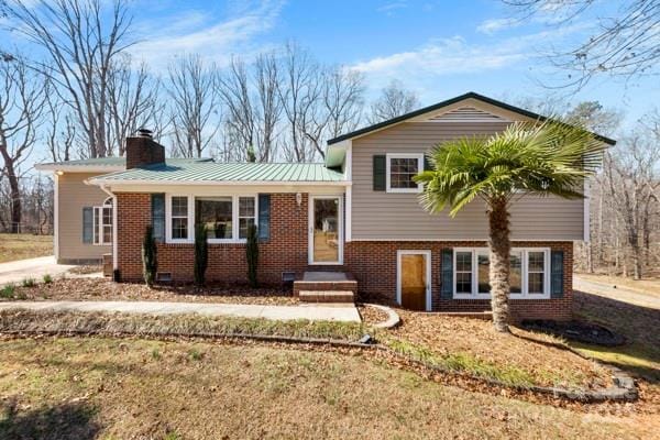 split level home with metal roof, brick siding, and a chimney