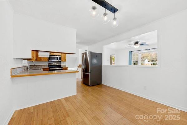 kitchen featuring stainless steel appliances, a peninsula, a sink, baseboards, and light wood-type flooring