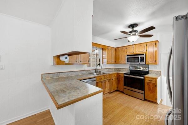 kitchen with a ceiling fan, appliances with stainless steel finishes, a peninsula, light wood-style floors, and a sink