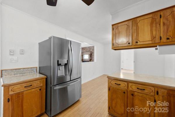 kitchen featuring ceiling fan, light wood-style flooring, light countertops, stainless steel fridge with ice dispenser, and brown cabinetry