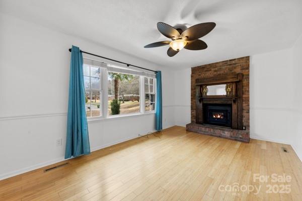 unfurnished living room with a ceiling fan, a fireplace, visible vents, and wood finished floors