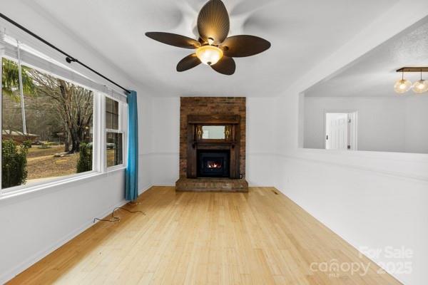 unfurnished living room with a wealth of natural light, a brick fireplace, ceiling fan, and wood finished floors