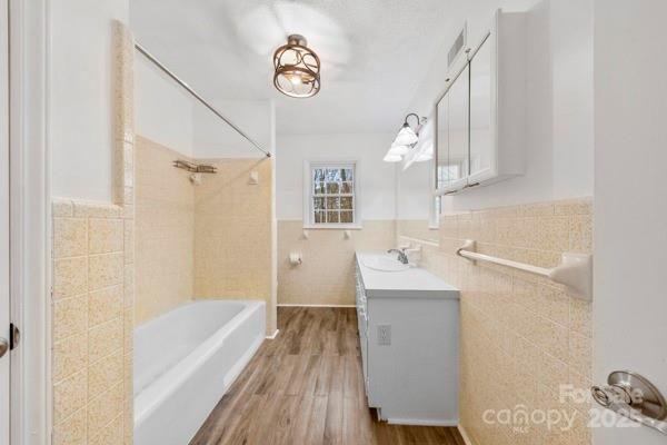 full bathroom with shower / bath combination, wood finished floors, vanity, tile walls, and wainscoting