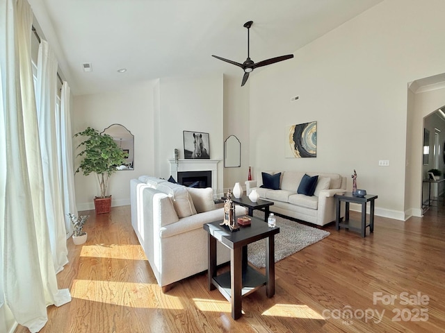 living area featuring a fireplace, visible vents, a ceiling fan, wood finished floors, and baseboards