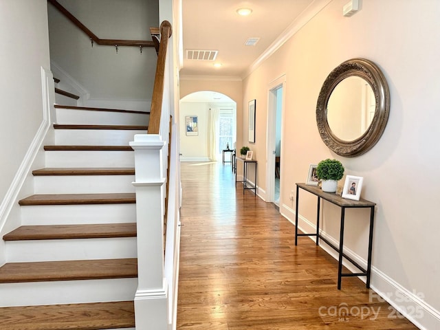 staircase featuring baseboards, visible vents, arched walkways, ornamental molding, and wood finished floors