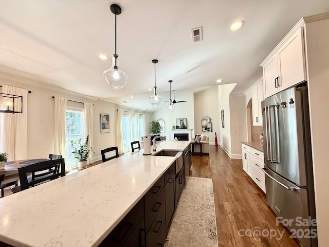 kitchen featuring visible vents, white cabinets, a large island, high quality fridge, and a sink