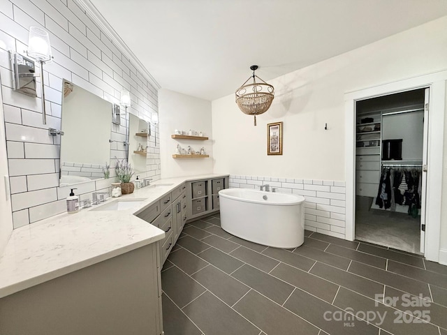 bathroom featuring a freestanding tub, a wainscoted wall, vanity, tile walls, and a spacious closet