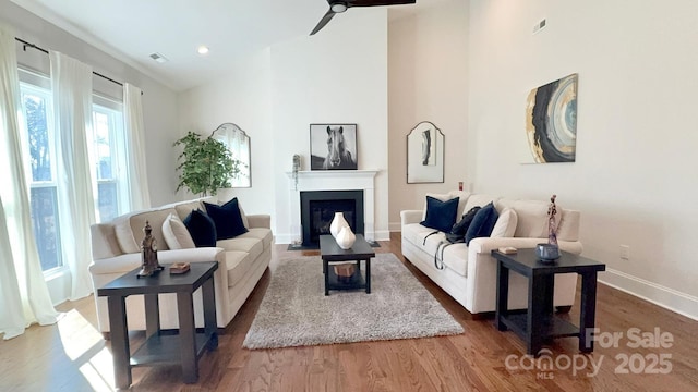 living area with high vaulted ceiling, a fireplace with flush hearth, visible vents, and wood finished floors