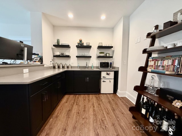 bar featuring a sink, baseboards, light wood-style floors, stainless steel microwave, and indoor wet bar