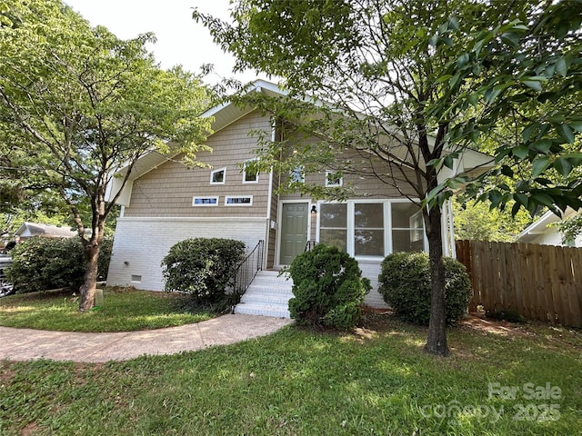 view of front of property with brick siding, crawl space, a front lawn, and fence